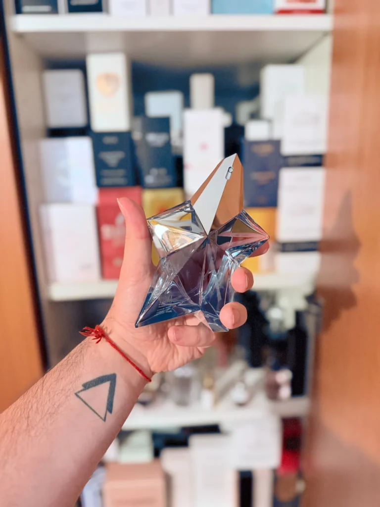 Mugler Angel perfume bottle held in hand in front of a fragrance collection