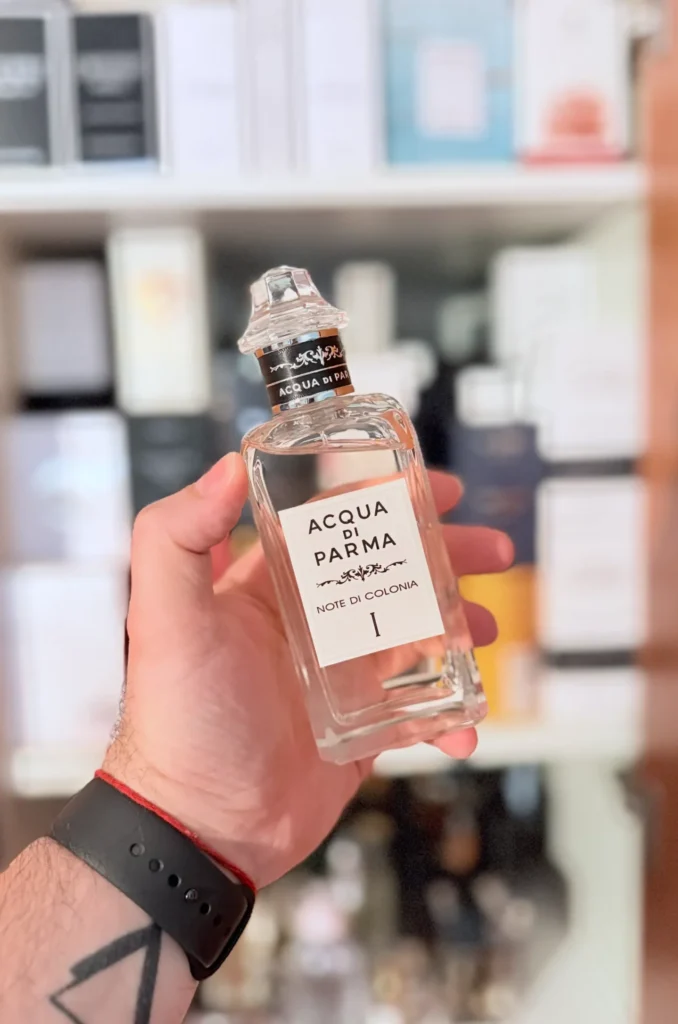 Hand holding an Acqua di Parma Note di Colonia I bottle in front of a perfume collection