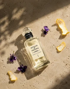 Acqua di Parma Note di Colonia I review cover with the perfume bottle, violet flowers and citrus peel in sunlight