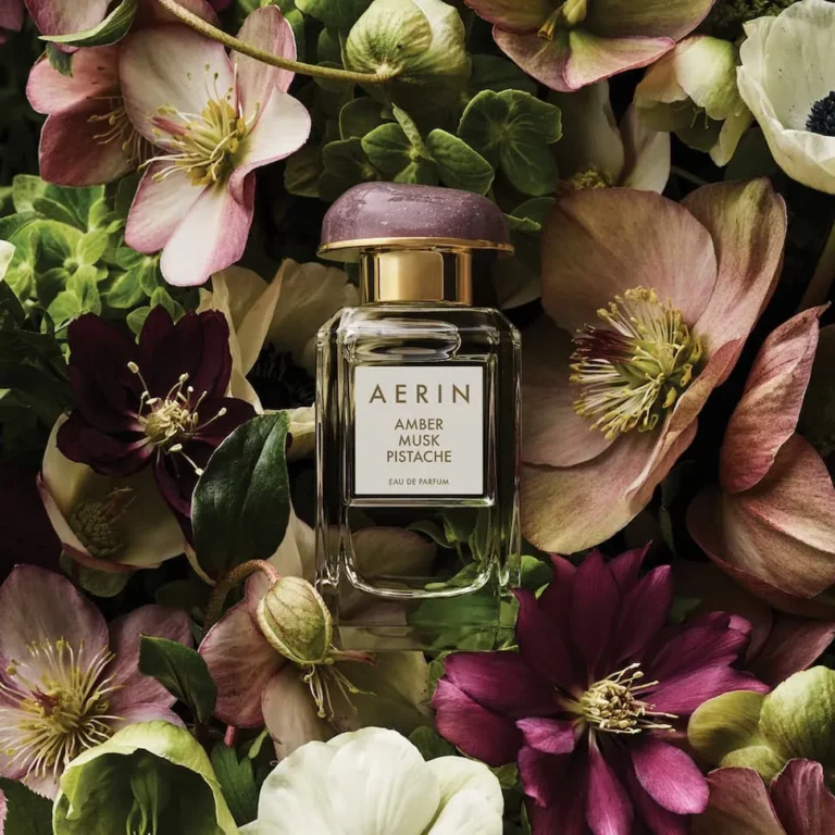 AERIN Amber Musk Pistache perfume bottle surrounded by pink, burgundy and cream flowers