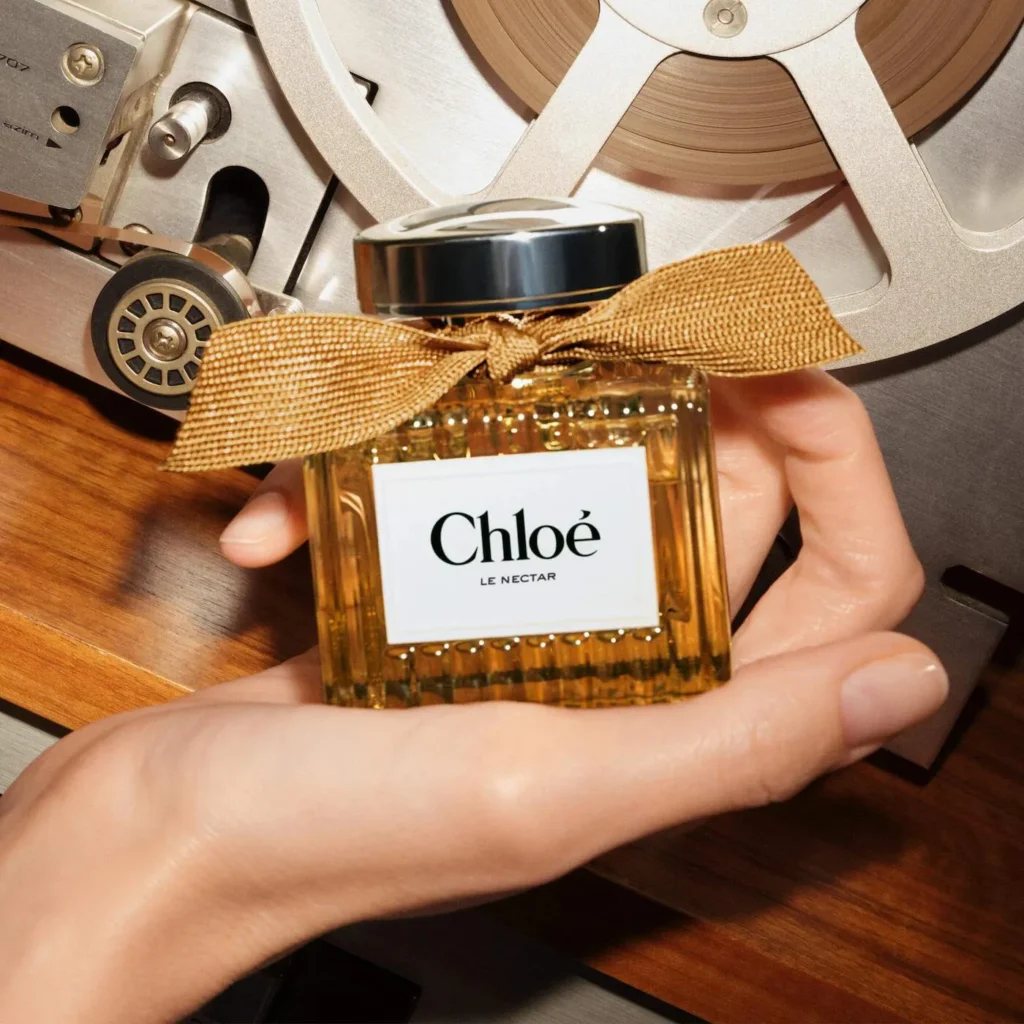 Chloé Le Nectar perfume bottle held in front of a reel to reel recorder