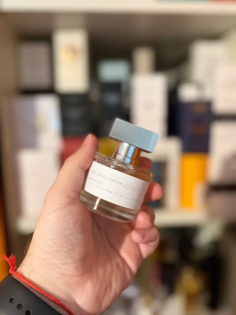 Hand holding a bottle of eRosion by Not Compliance Studio in front of a perfume collection