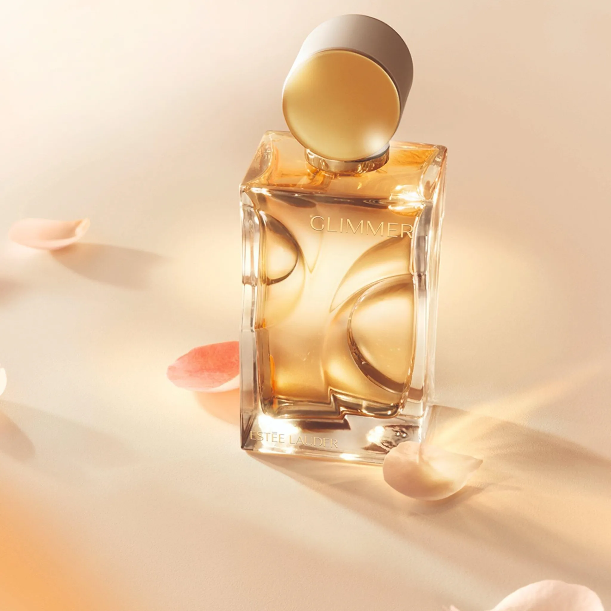 Estée Lauder Glimmer perfume bottle glowing in warm golden light with rose petals