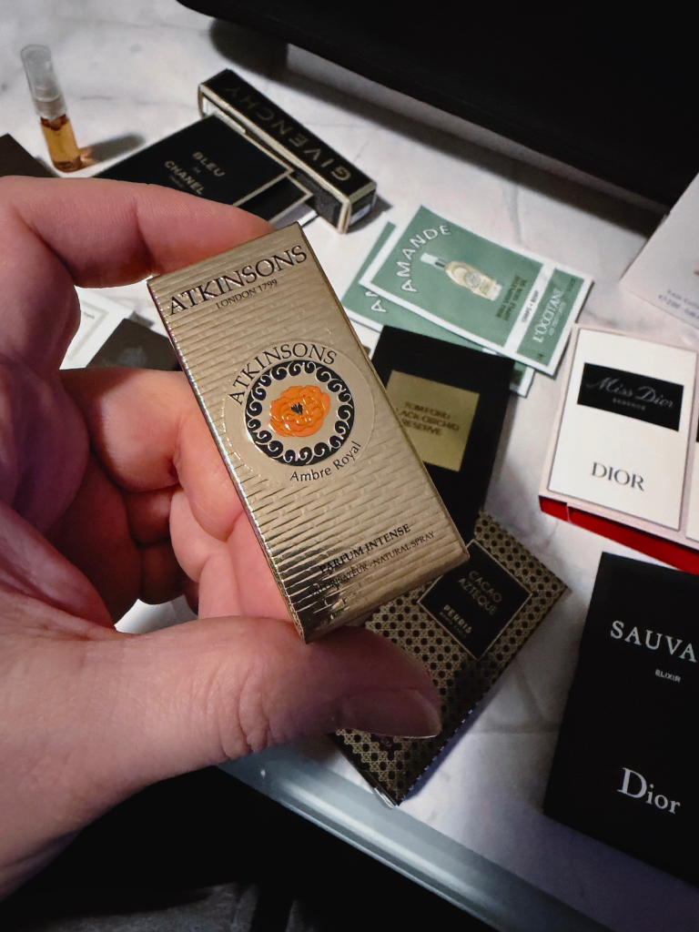 Hand holding an Atkinsons Ambre Royal perfume sample box with more fragrance samples blurred in the background