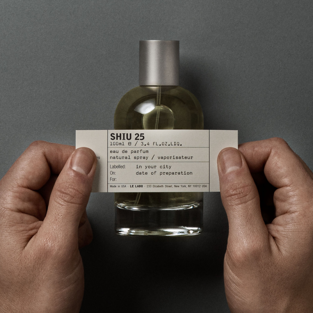 Hands holding a personalised Le Labo Shiu 25 label in front of the perfume bottle.
