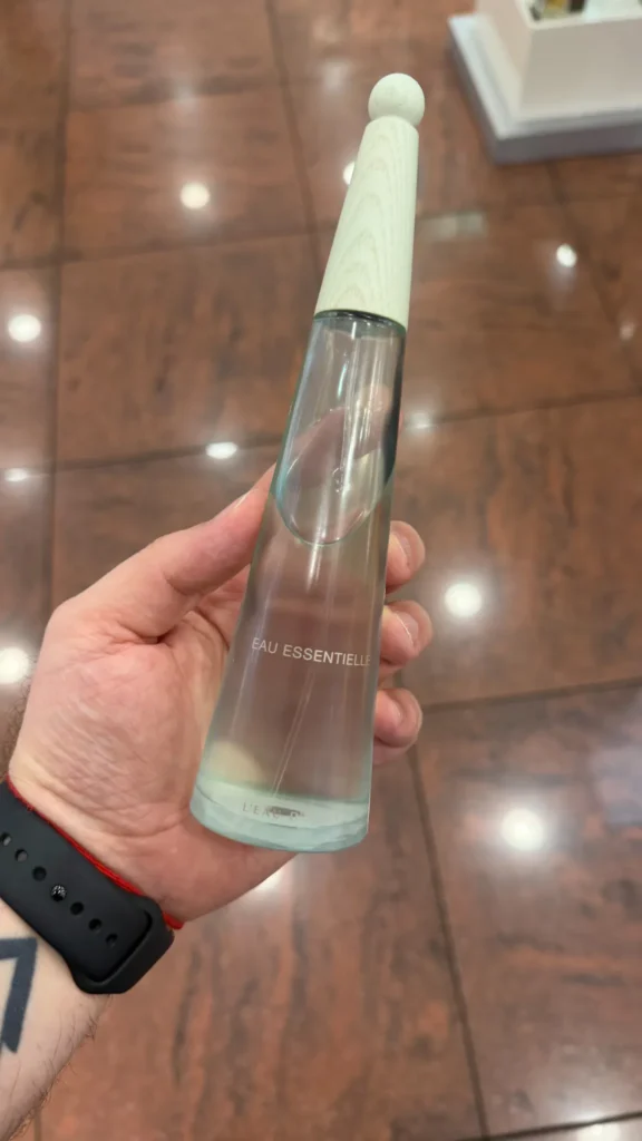 L’Eau d’Issey Eau Essentielle perfume bottle held in hand inside a store