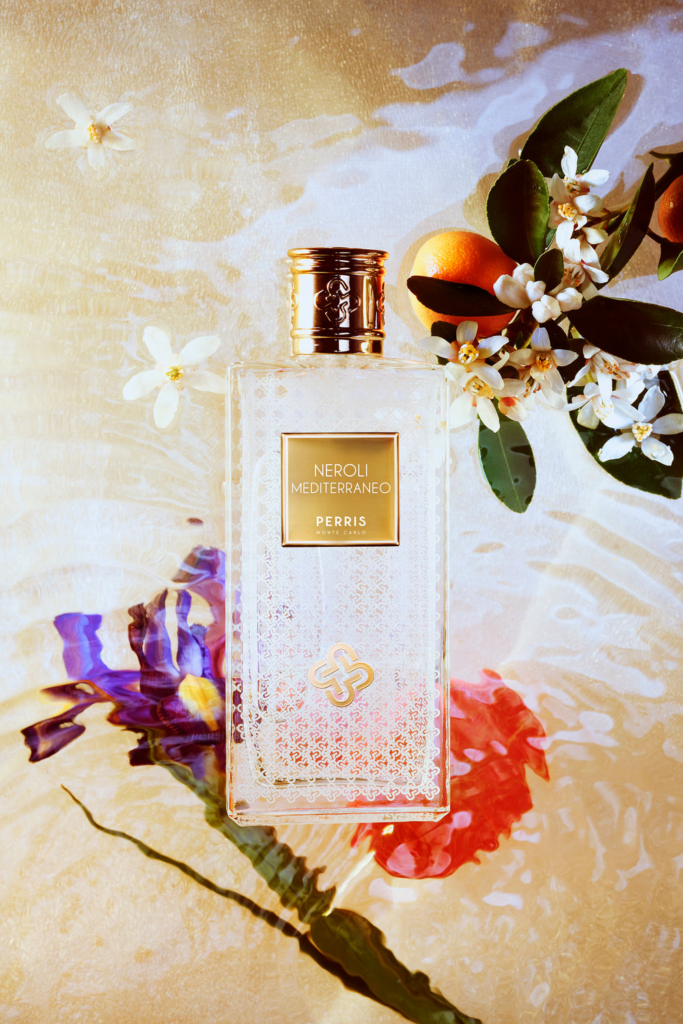 Perris Monte Carlo Neroli Mediterraneo bottle surrounded by orange blossom, citrus and colorful reflections on water.