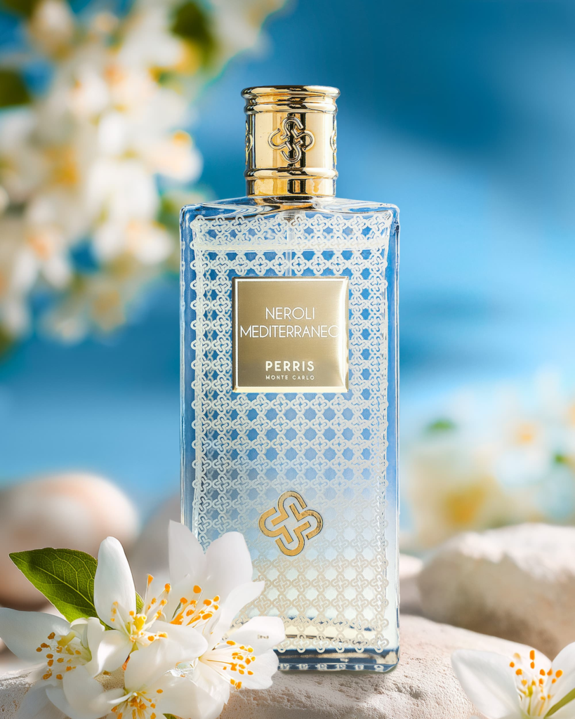 Perris Monte Carlo Neroli Mediterraneo bottle with white orange blossom against a bright blue Mediterranean background.