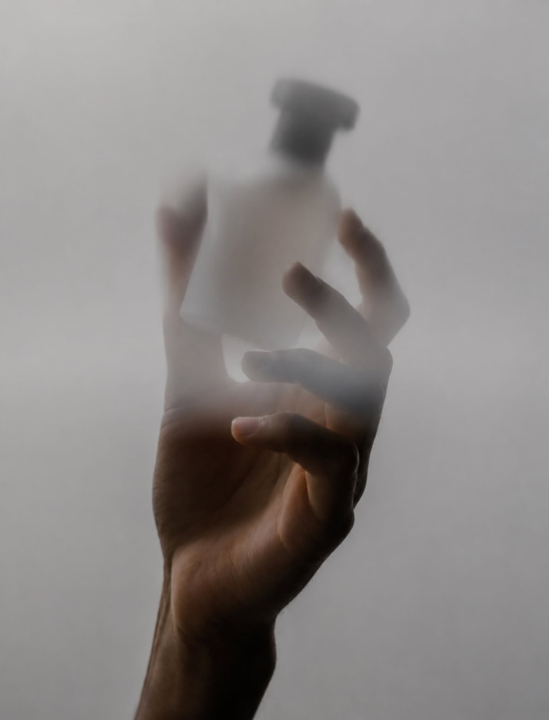 A hand holding the frosted Musk1920 perfume bottle behind translucent fabric.