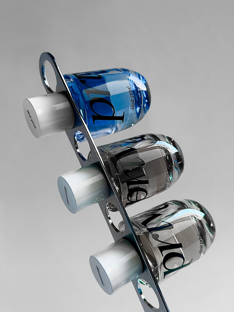 Blue and clear Élixir Privé perfume bottles resting in sculptural metal holders.