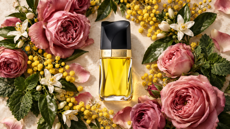 Estée Lauder Knowing bottle surrounded by roses, mimosa, orange blossom and patchouli leaves