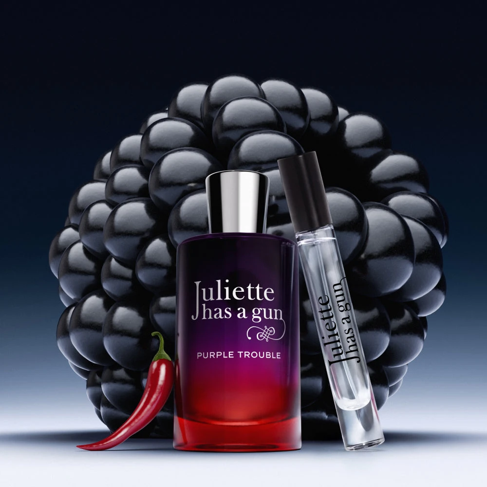 Purple Trouble perfume bottle and travel spray in front of a blackberry with a red chilli pepper