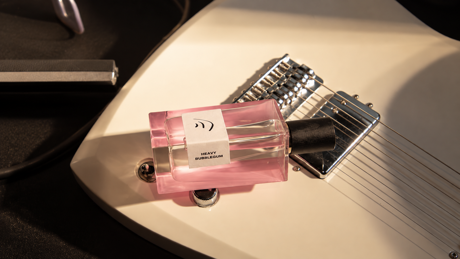 Pink Heavy Bubblegum perfume bottle resting on a cream electric guitar