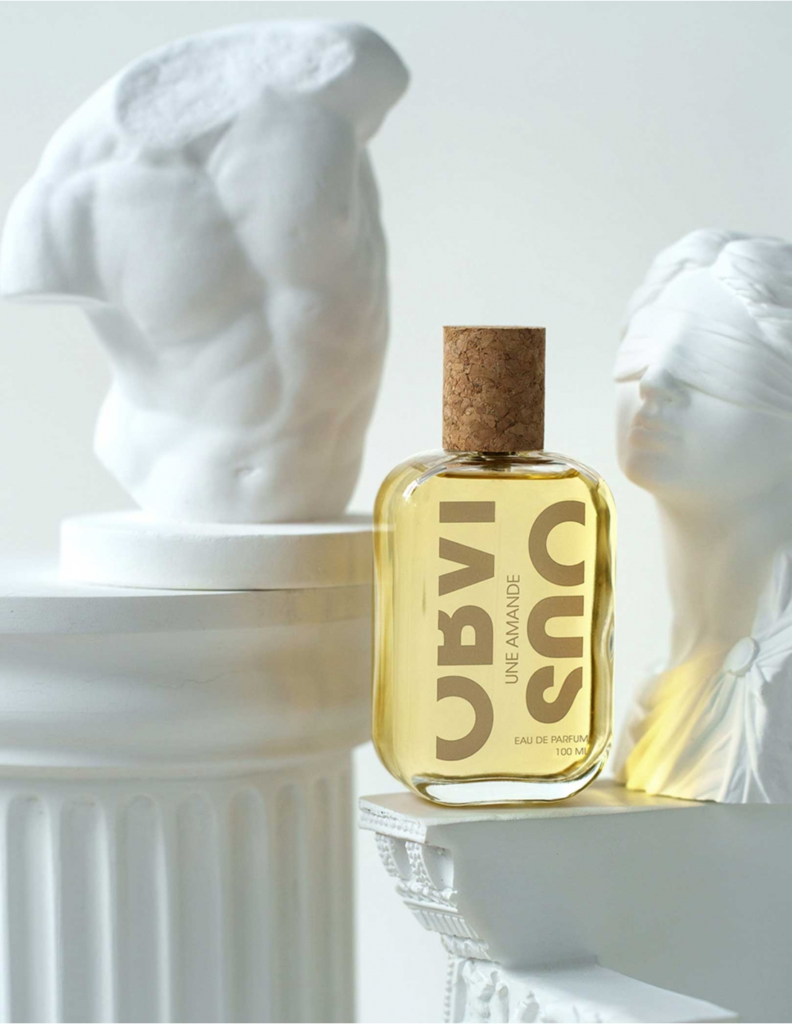 Obvious Une Amande perfume bottle displayed among white classical sculptures