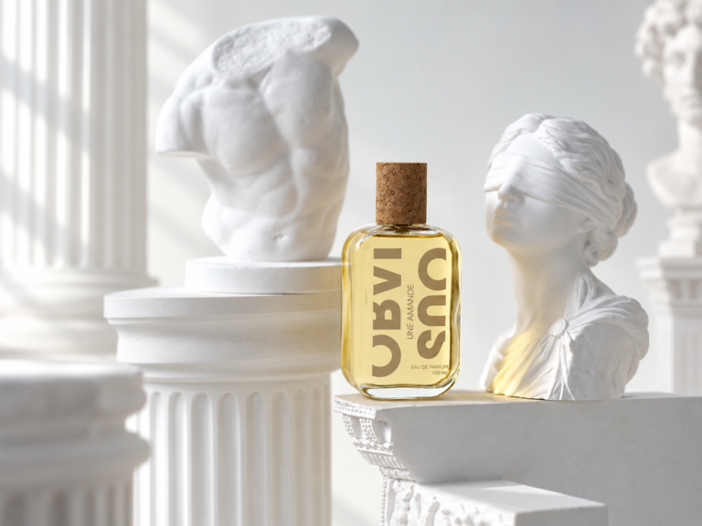Obvious Une Amande perfume bottle surrounded by white classical sculptures
