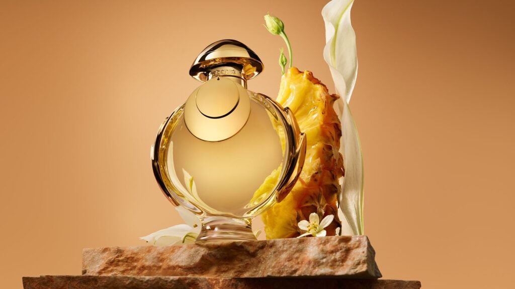 Rabanne Olympea Elixir bottle displayed with pineapple and white flowers