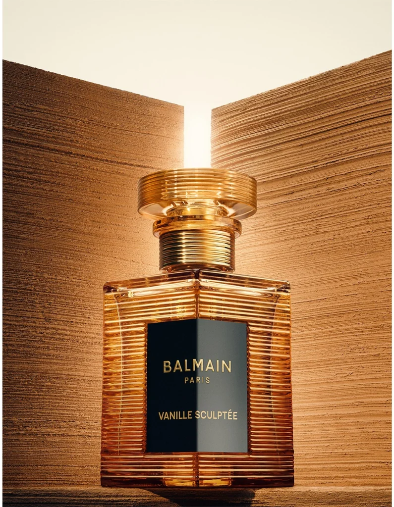 Balmain Vanille Sculptée bottle with ribbed amber glass and a black label between textured golden walls