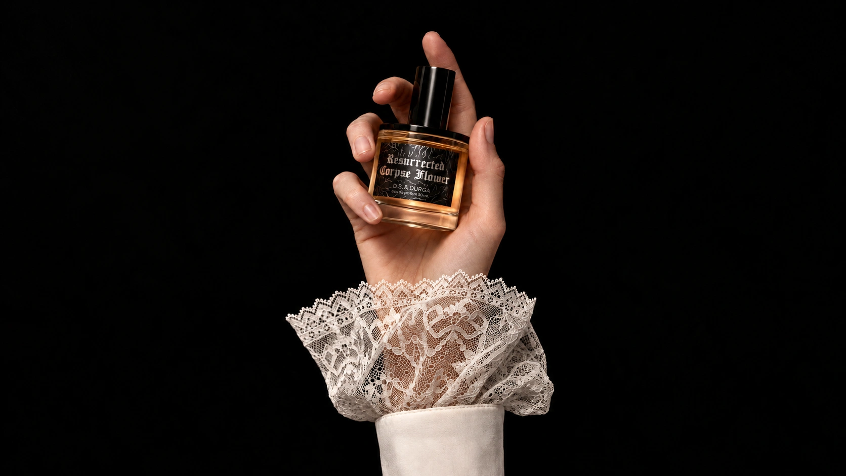 D.S. & DURGA Resurrected Corpse Flower perfume bottle held by a hand wearing delicate white lace against a black background.
