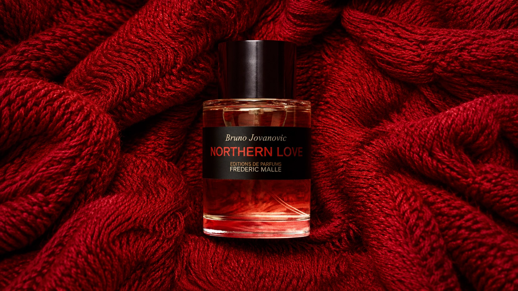 Frédéric Malle Northern Love perfume by Bruno Jovanovic resting on rich red knitted fabric.
