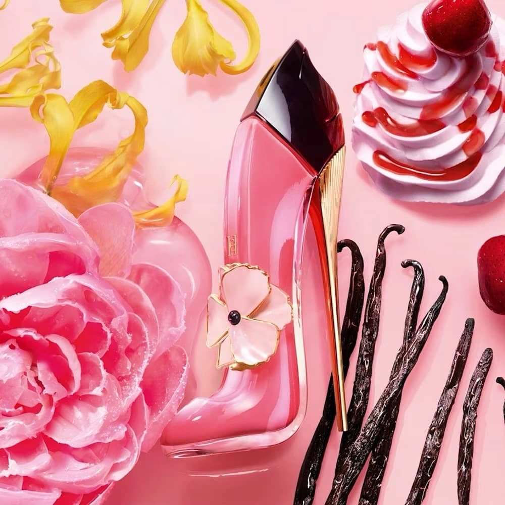 Carolina Herrera Good Girl Blush Delight pink perfume bottle surrounded by strawberries, whipped cream, vanilla pods and pink flowers.