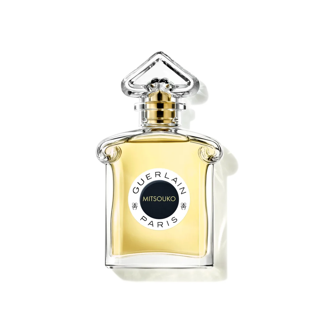 Guerlain Mitsouko Eau de Parfum bottle with pale golden liquid, an ornate transparent stopper and a circular black label.