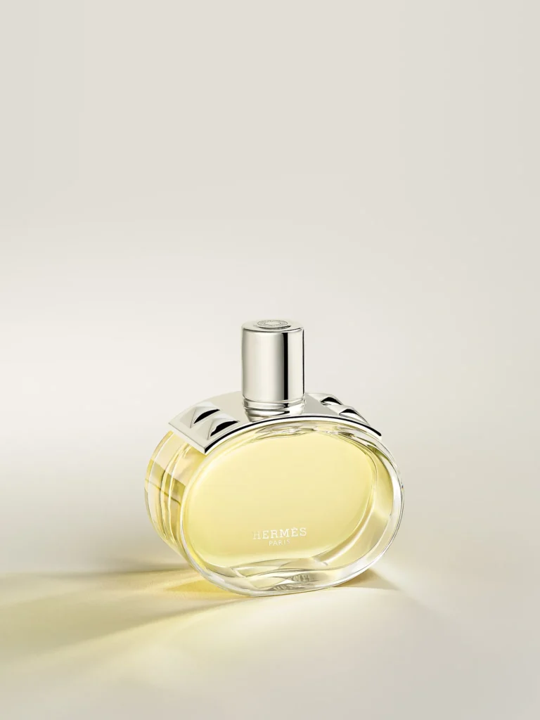 Hermès Barénia Eau de Parfum bottle with its oval glass design, pale golden liquid and silver metallic details.