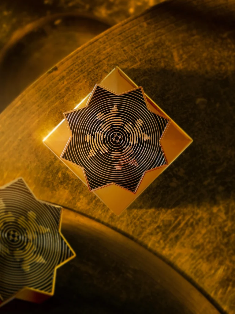 Geometric eight-pointed star designs with concentric patterns in gold and black, photographed for Kajal Perfumes.