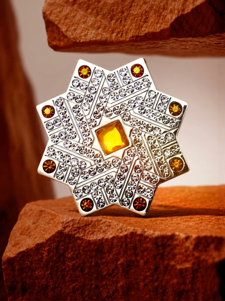Ornate silver eight-pointed star with sparkling crystals and amber-colored stones, photographed for Kajal Perfumes.