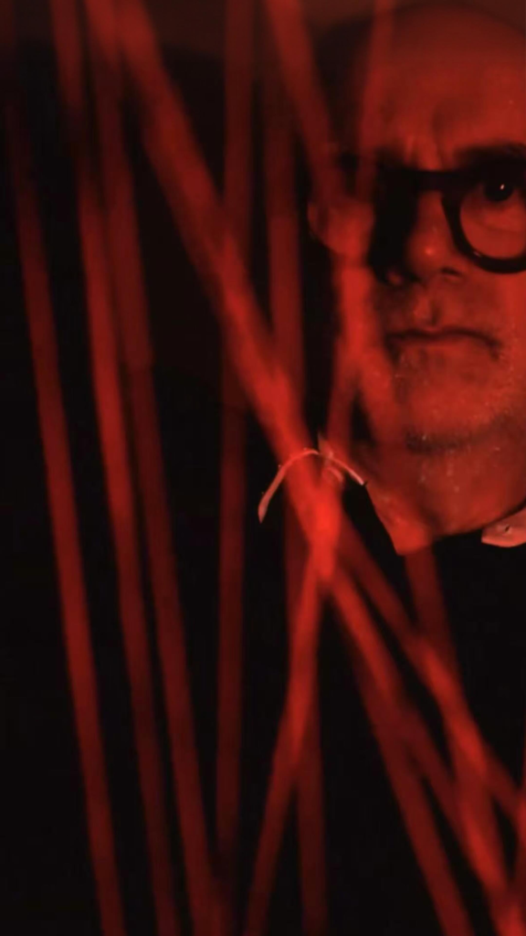 Perfumer portrait lit in red behind sculptural branches