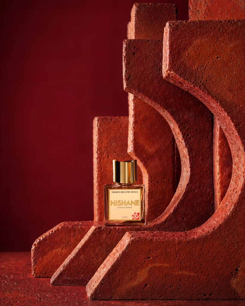 Nishane Thorns Become Roses bottle among curved terracotta structures and textured red steps