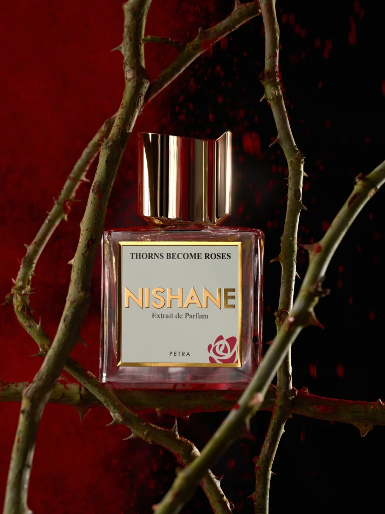 Nishane Thorns Become Roses bottle framed by thorn branches against a dark red background
