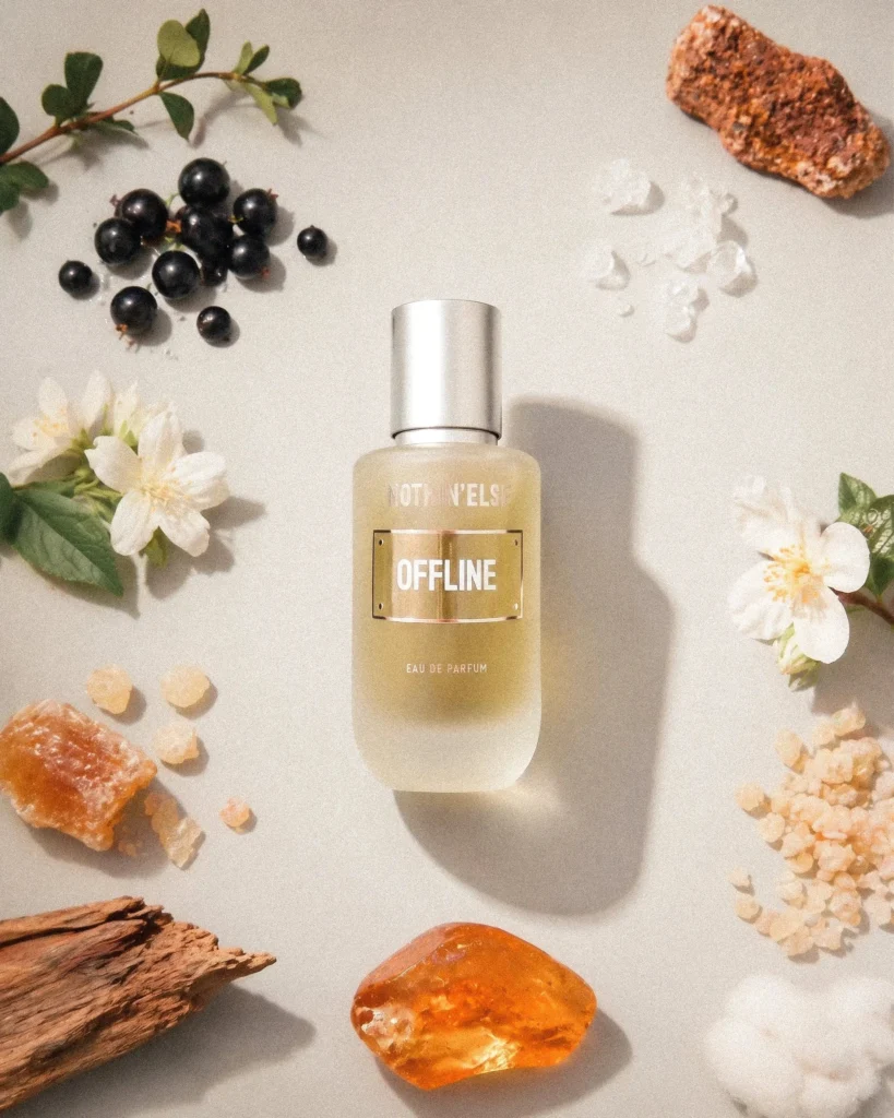NOTHIN’ELSE Offline bottle surrounded by dark berries, white flowers, wood and amber-coloured pieces