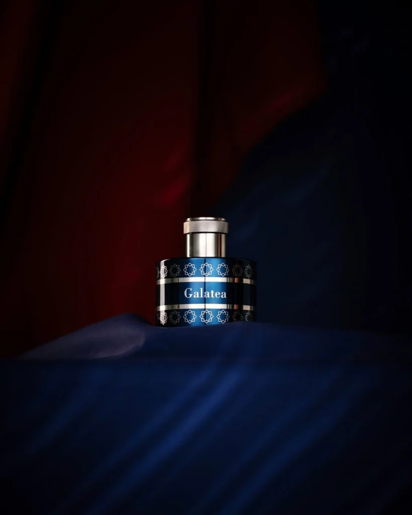 Pantheon Roma Galatea perfume bottle emerging from dark blue fabric with dramatic burgundy and navy lighting.