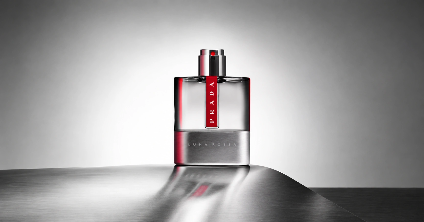 Prada Luna Rossa Eau de Toilette bottle on a metallic surface with soft reflections and a grey background.