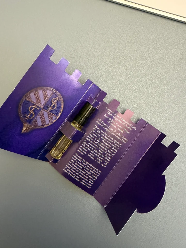 V Canto Isotta perfume sample vial inside its unfolded purple presentation packaging.