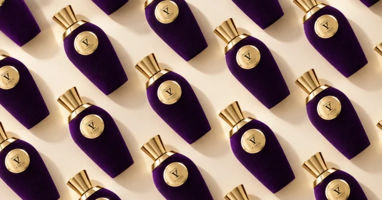Editorial composition featuring multiple purple V Canto Isotta perfume bottles with gold caps against a cream background.